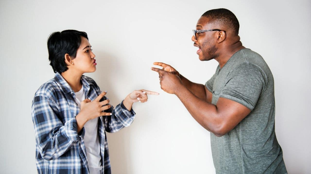 A man and woman argue, pointing at each other.