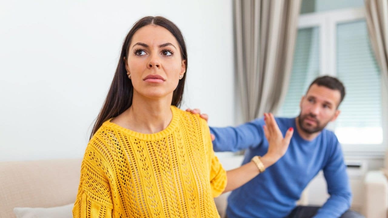A woman in a yellow sweater looks away from a man who is reaching out to her.