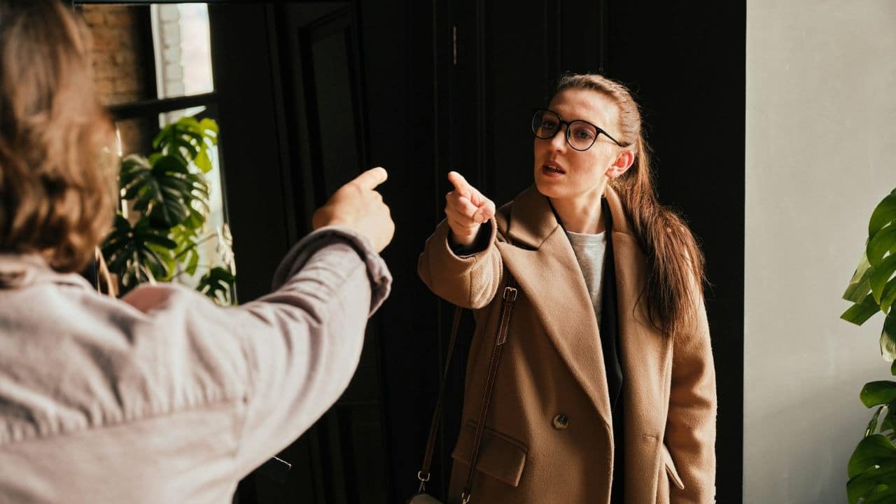 A woman with glasses argues and points at someone off-camera.