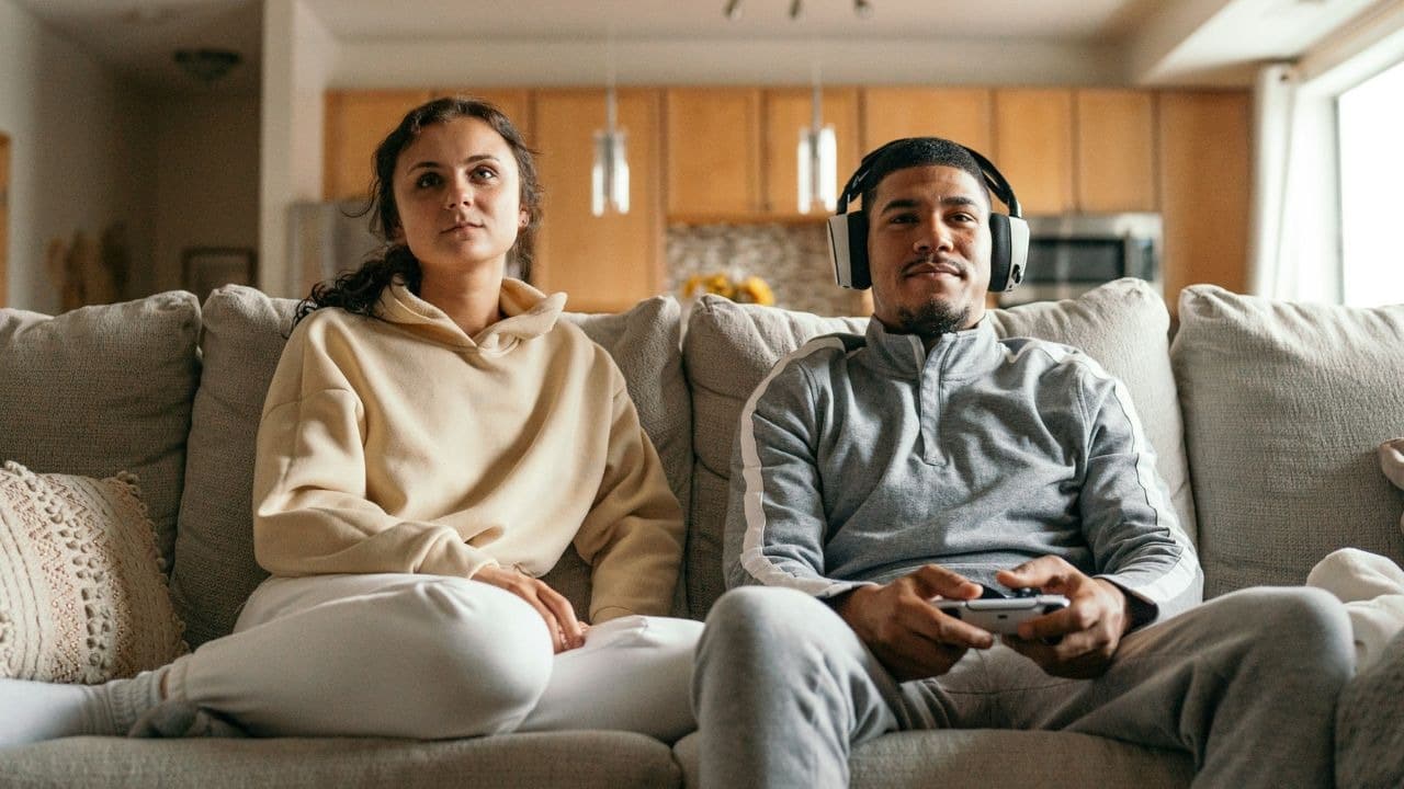 A bored woman sits next to a man who is intently focused on playing a video game.