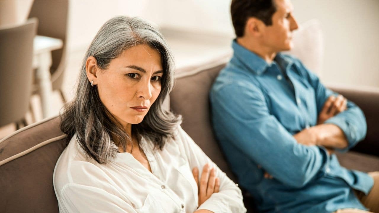 A frustrated woman with her arms crossed sits on a couch, looking away from a man.