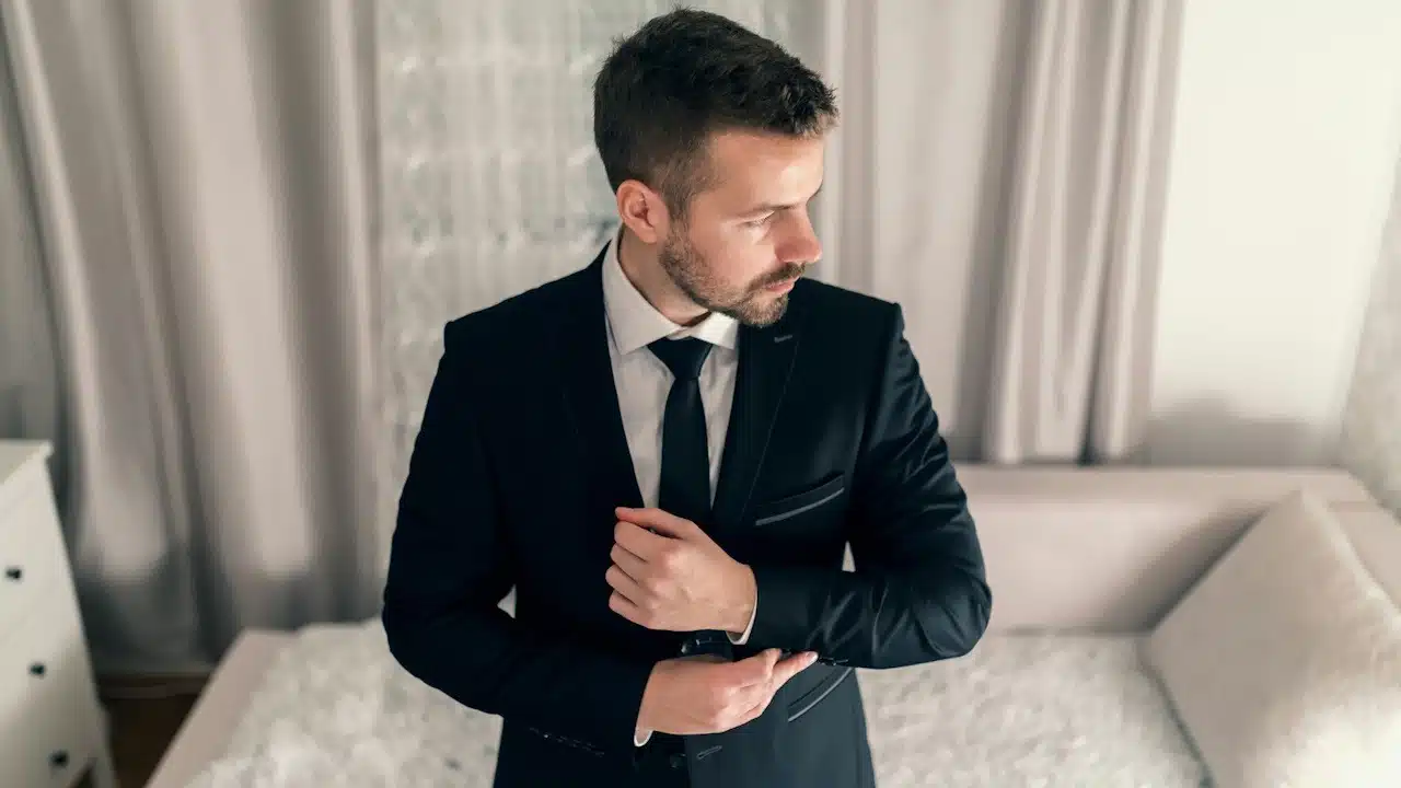 Young businessman tying cufflinks on jacket and looking away.