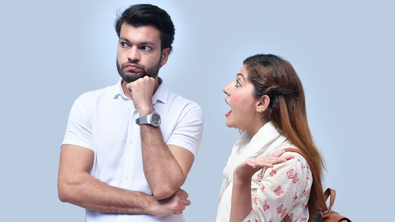 A woman shouting at a bearded man who looks to the side with a controlled expression.