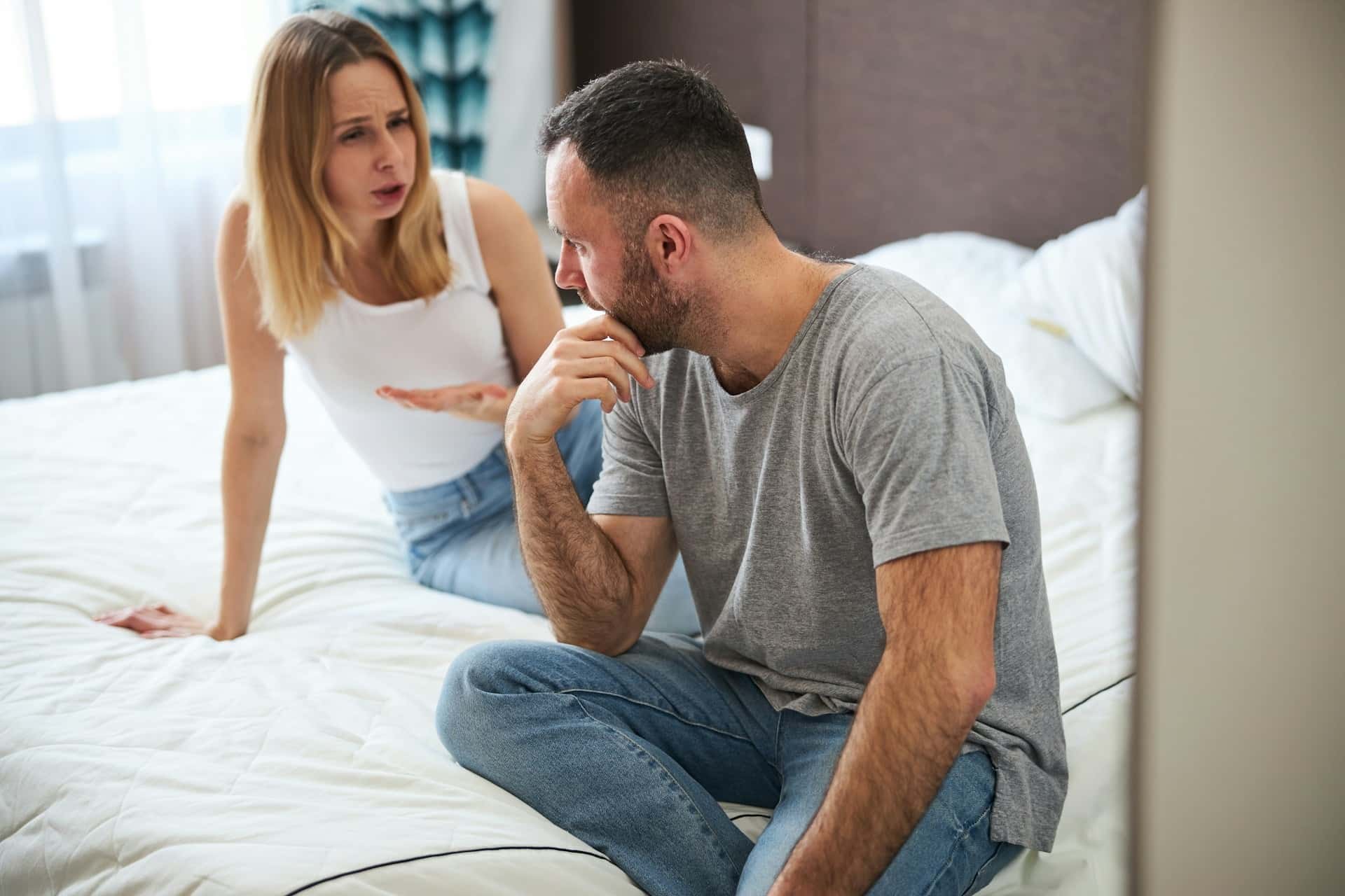 A woman complaining to a man who looks vacuous while they sit on a bed.