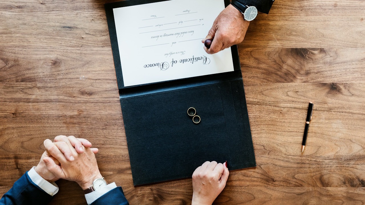 An overhead view of three people sitting at a table while a lawyer stamps a divorce certificate.