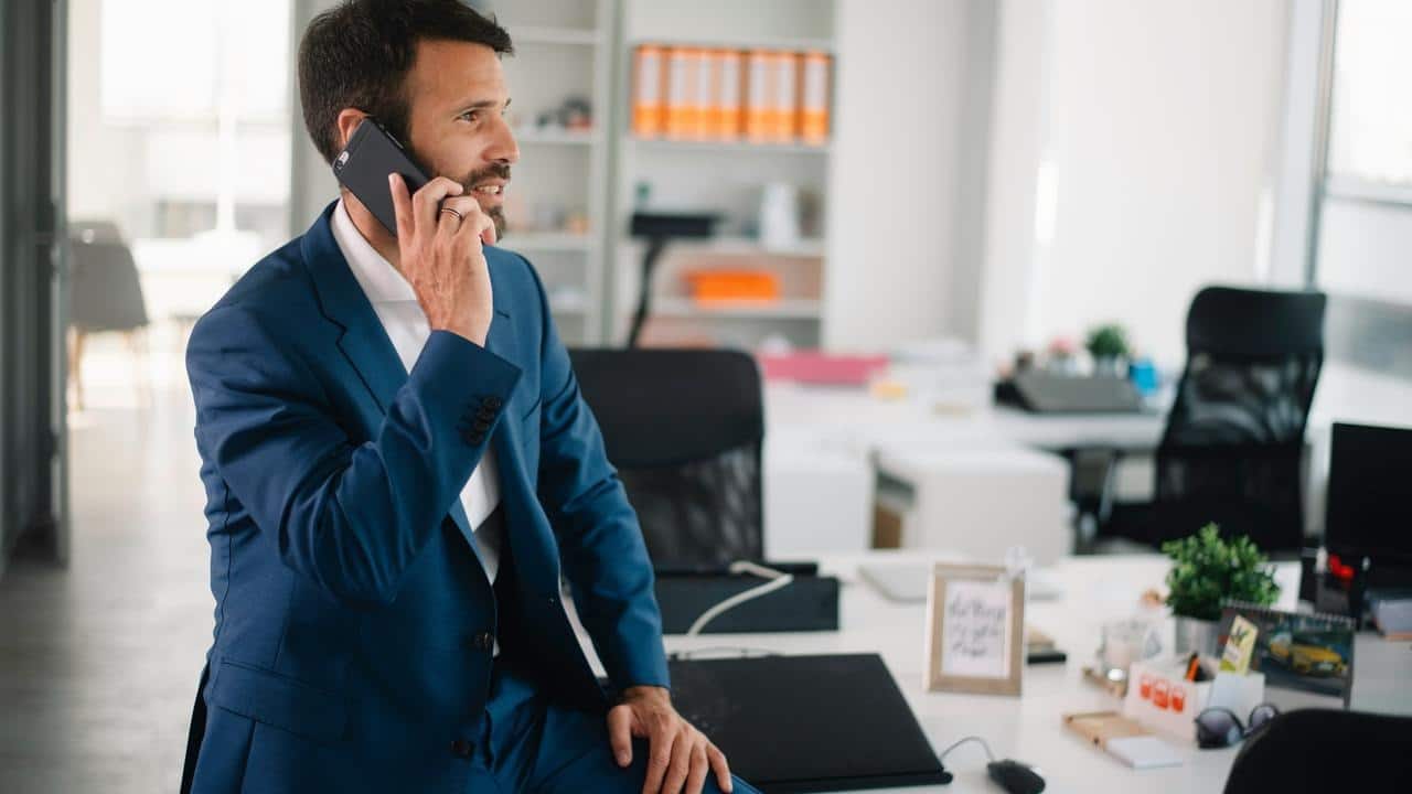 A man in a suit talking on a phone in a modern office.