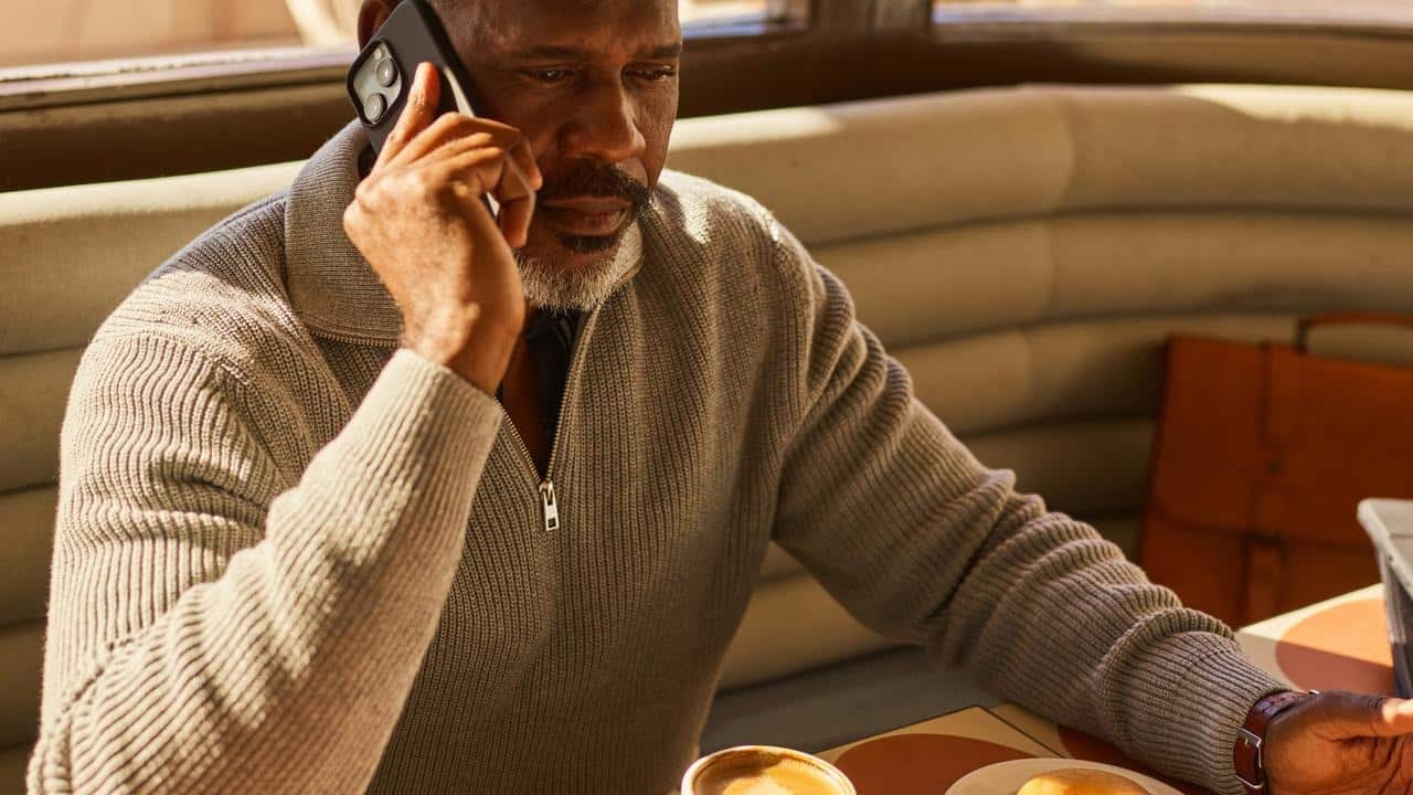 A man talking on a phone while sitting at a café table with coffee.