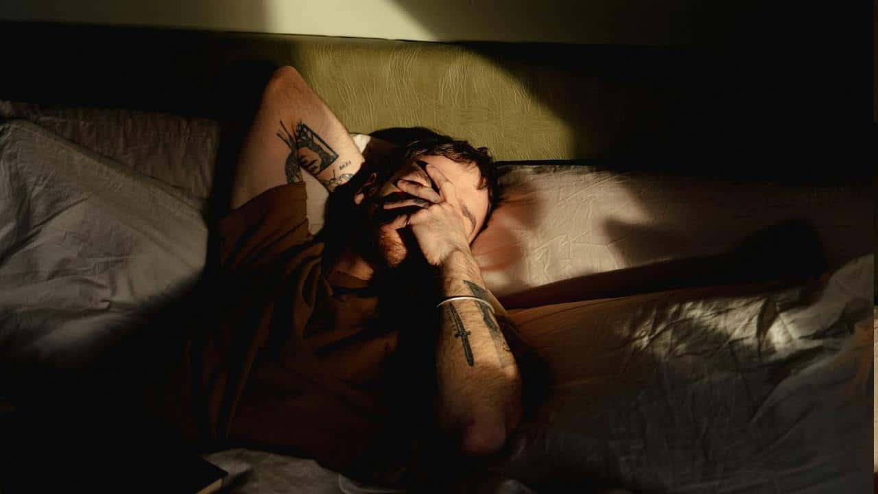 A man lying in bed with his head on his hands.