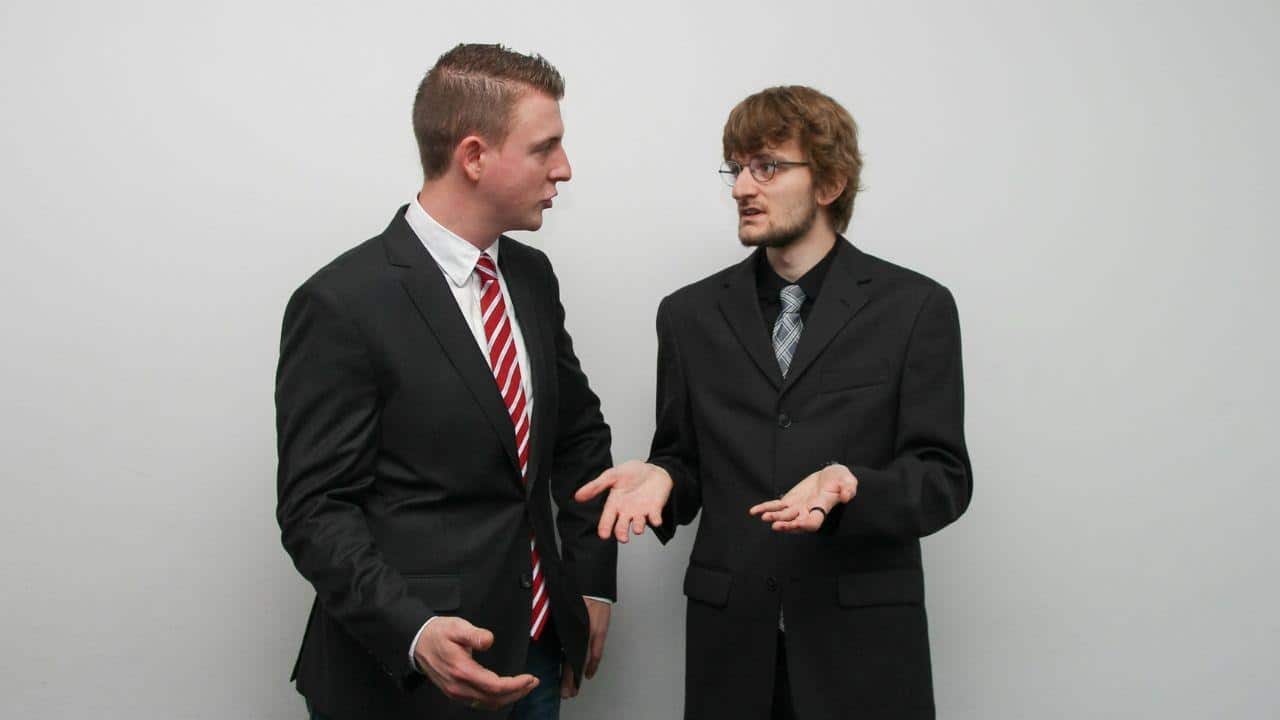 Two men in business suits having an animated conversation against a white background.