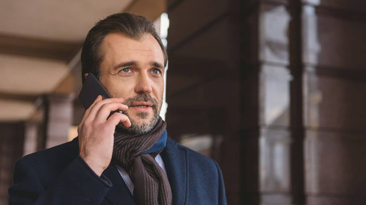 Man with a beard and a scarf talking on a cell phone outdoors.
