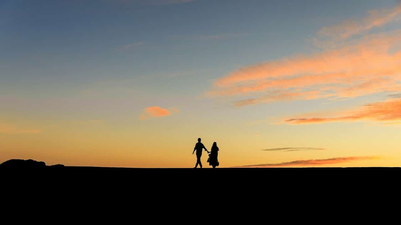 A couple walking while holding hands at sunset.