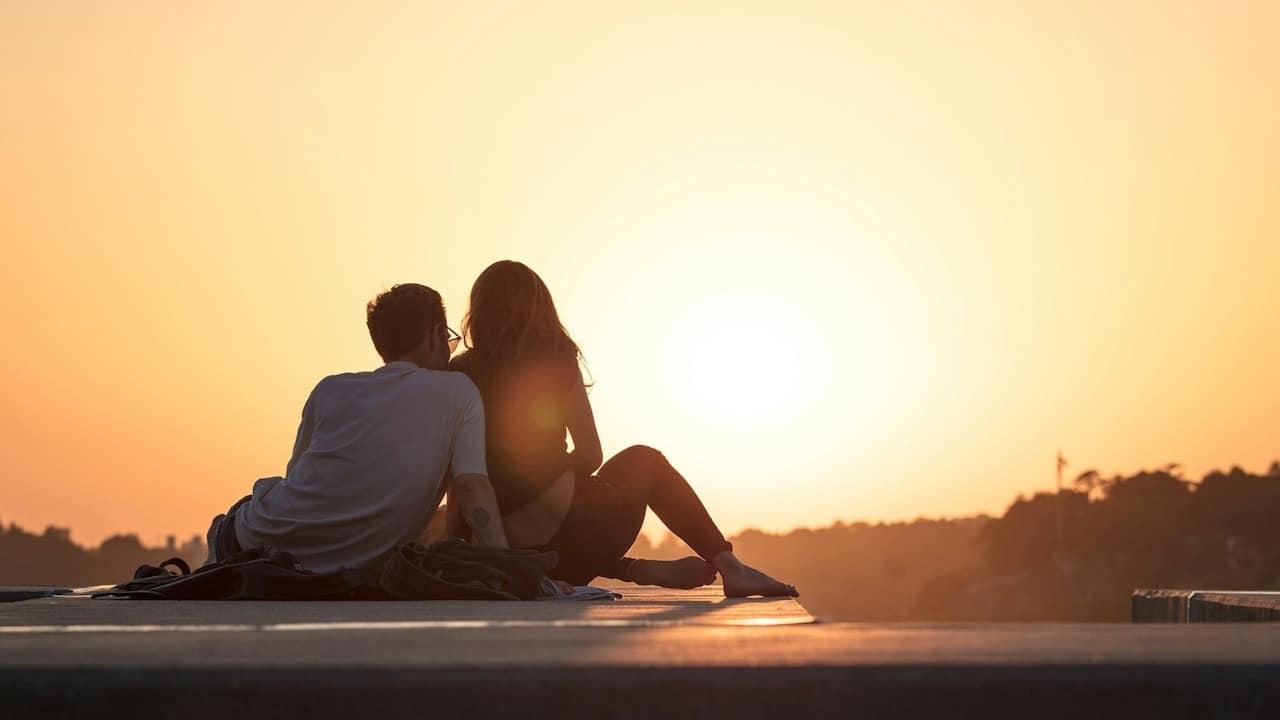 A couple sitting together outdoors at sunset.