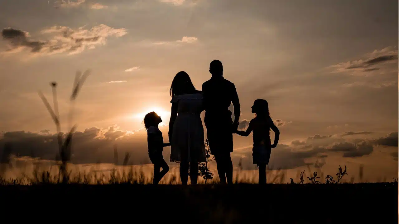 A picture of a family’s silhouette while they stand outdoors at sunset.