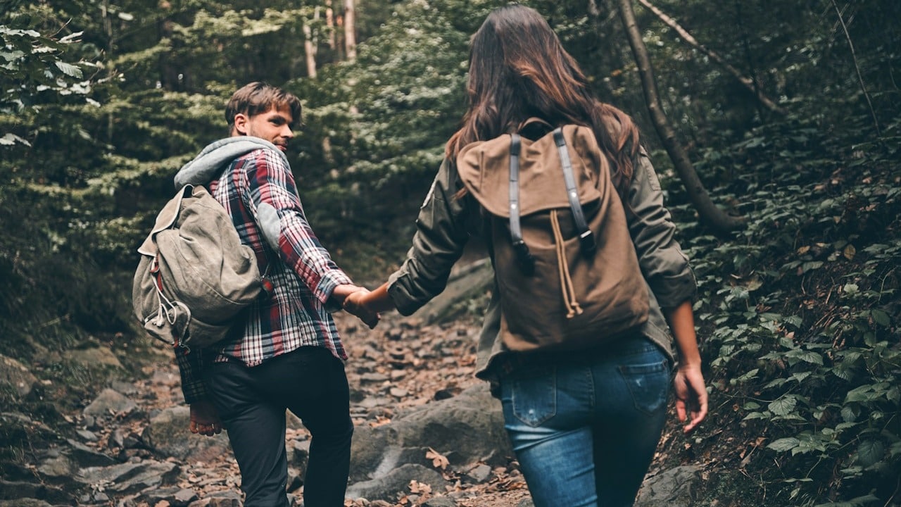 A couple hiking together, with the man supporting the woman by holding her hand as she climbs.
