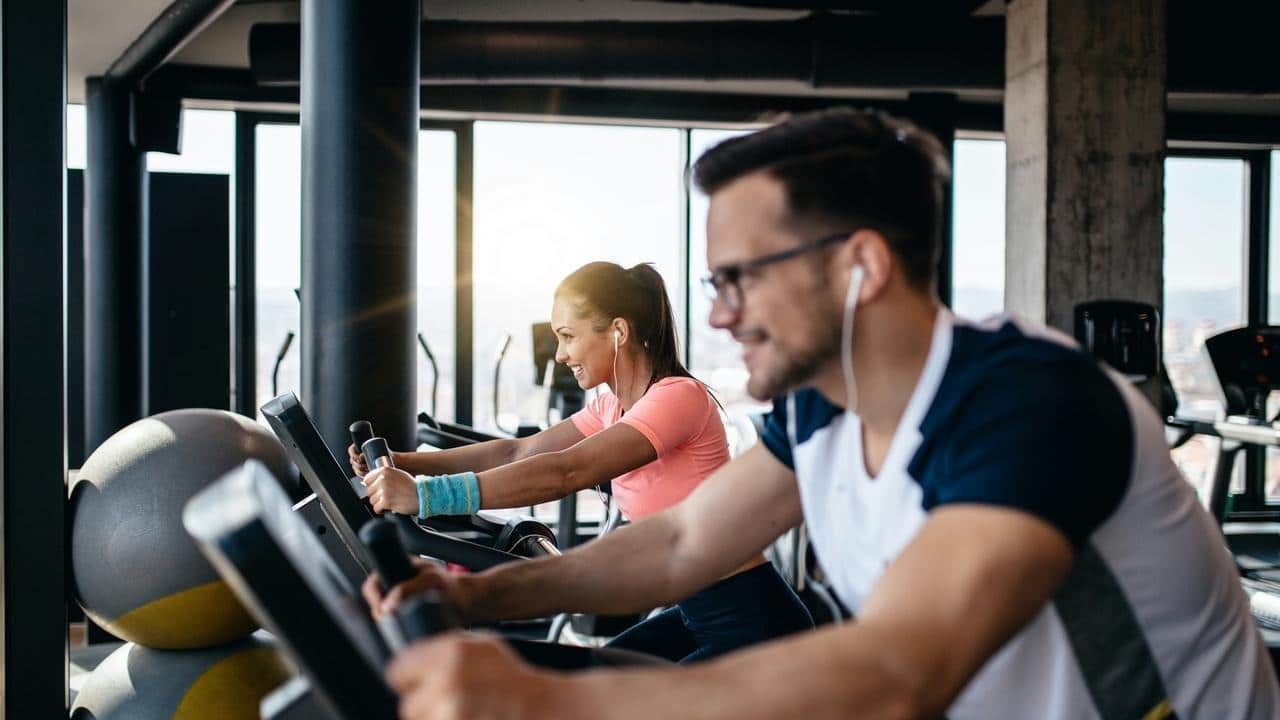 A man and woman exercising on stationary bikes at a gym.