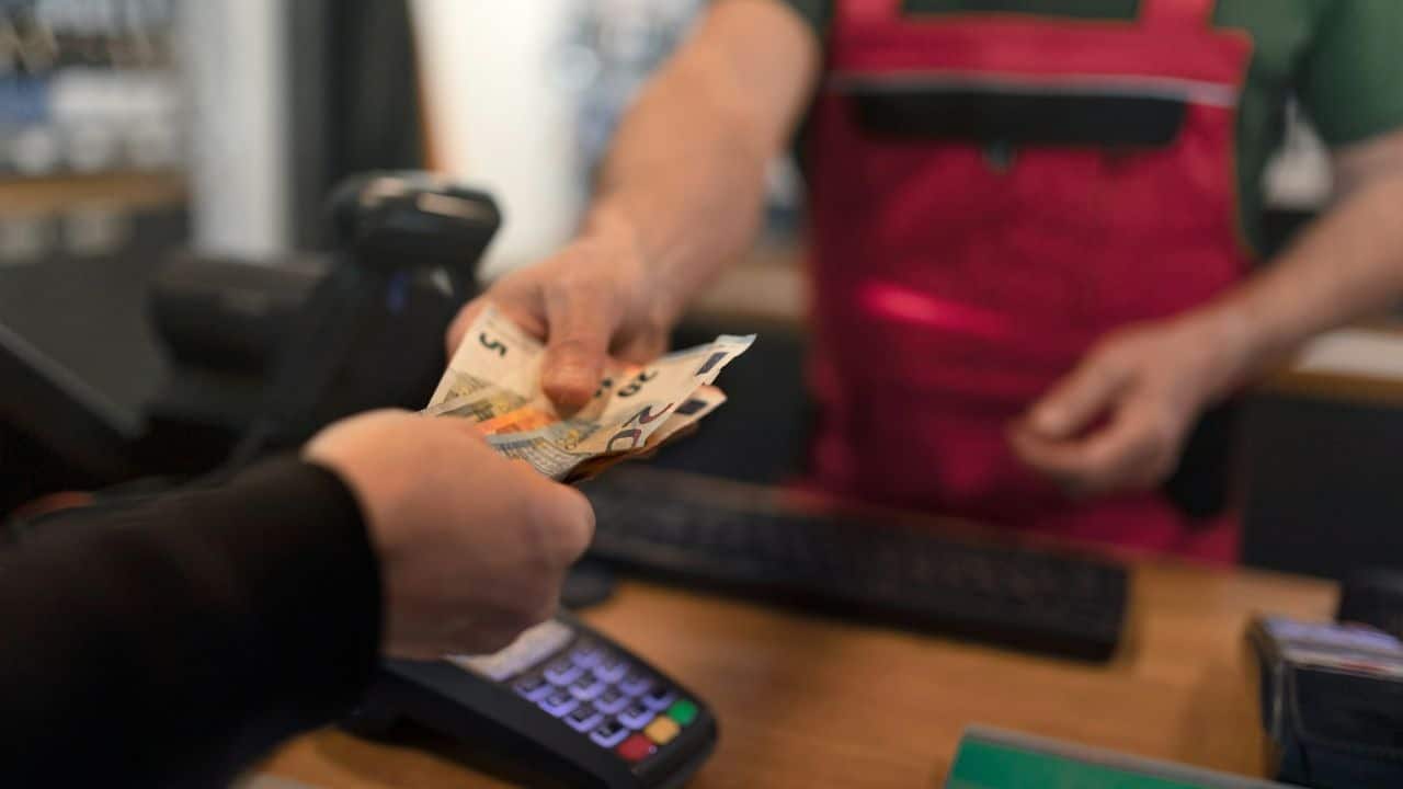 A customer's hand is giving a cashier some Euro currency notes.