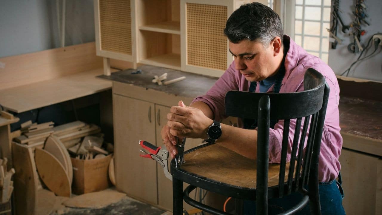 A man is working on a wooden chair using pliers in his workshop.