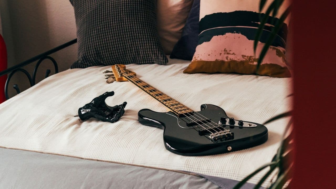 A black electric bass guitar and a black sculpture of a hand are lying on a bed.