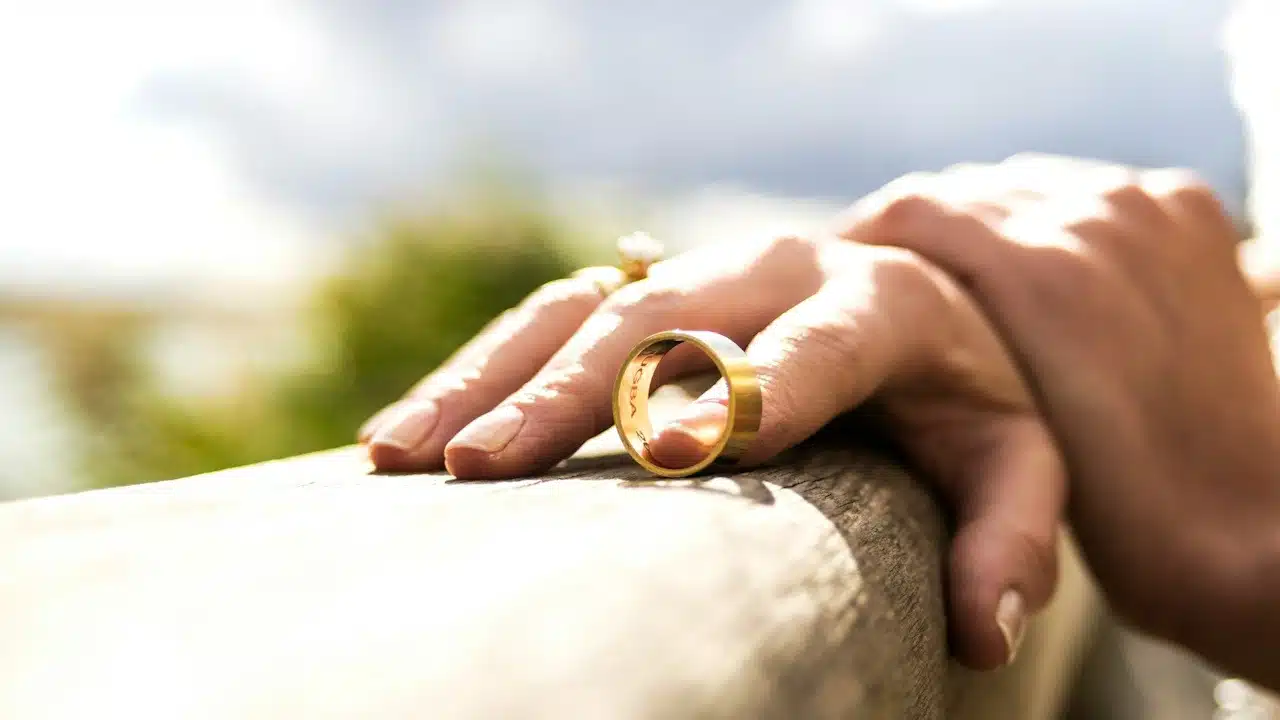 A person holding their wedding ring with a finger while it is placed on a wooden surface.