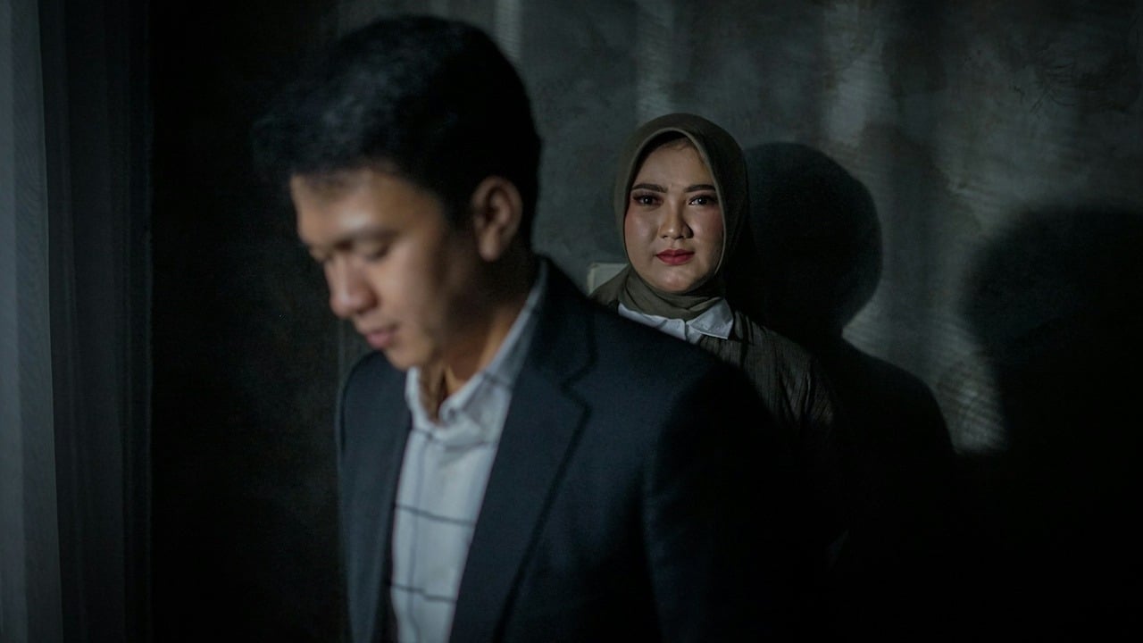 A woman wearing a head scarf standing behind a man who is looking down.