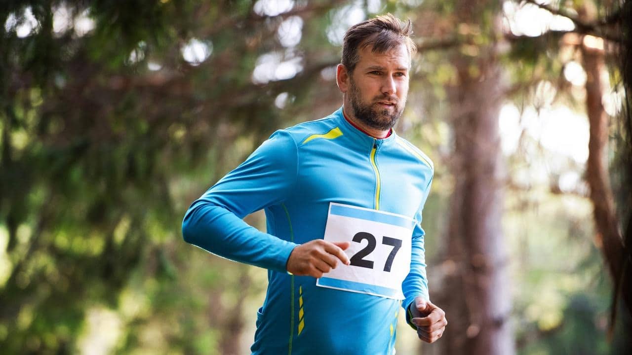 A man running outdoors wearing a blue sports outfit with a race number.