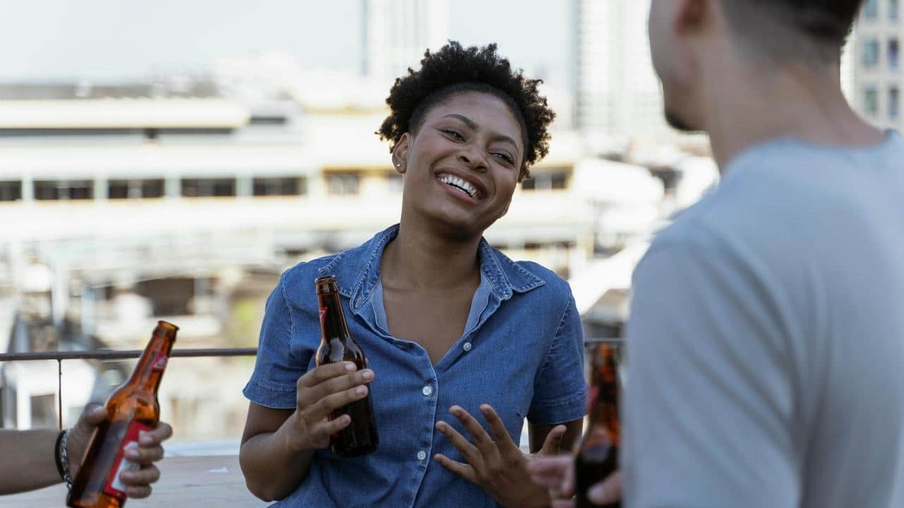 A woman laughing while holding a beer bottle during a rooftop gathering.