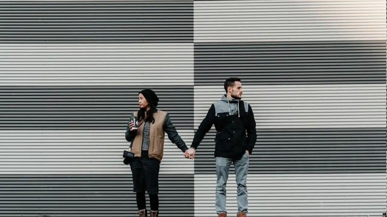 A man and woman looking away while holding each other's hands.