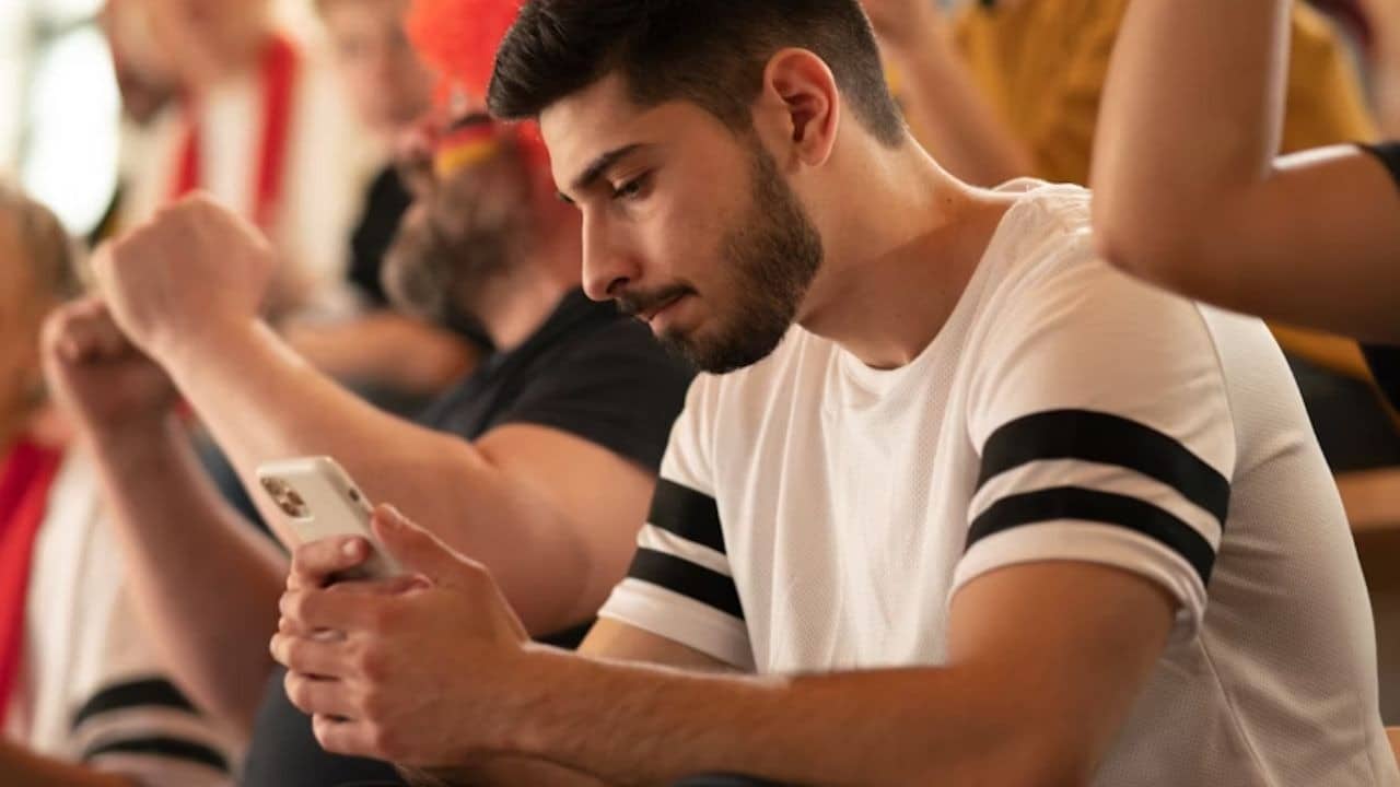 Man scrolling his phone while appearing preoccupied in a social setting