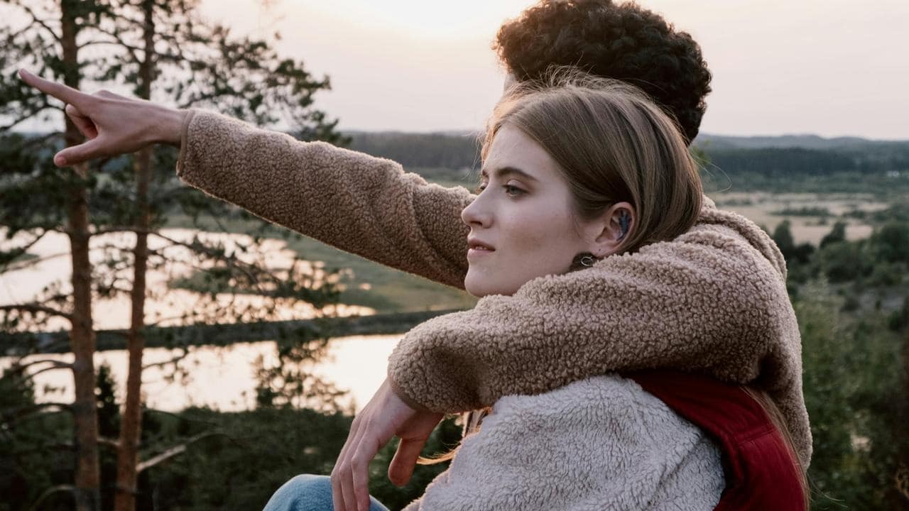 A couple sitting outdoors at sunset, with one person pointing into the distance.