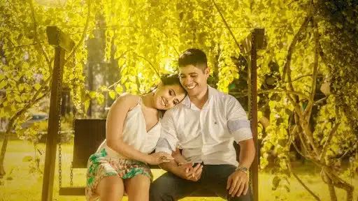 A man and a woman sitting on a swing in nature.