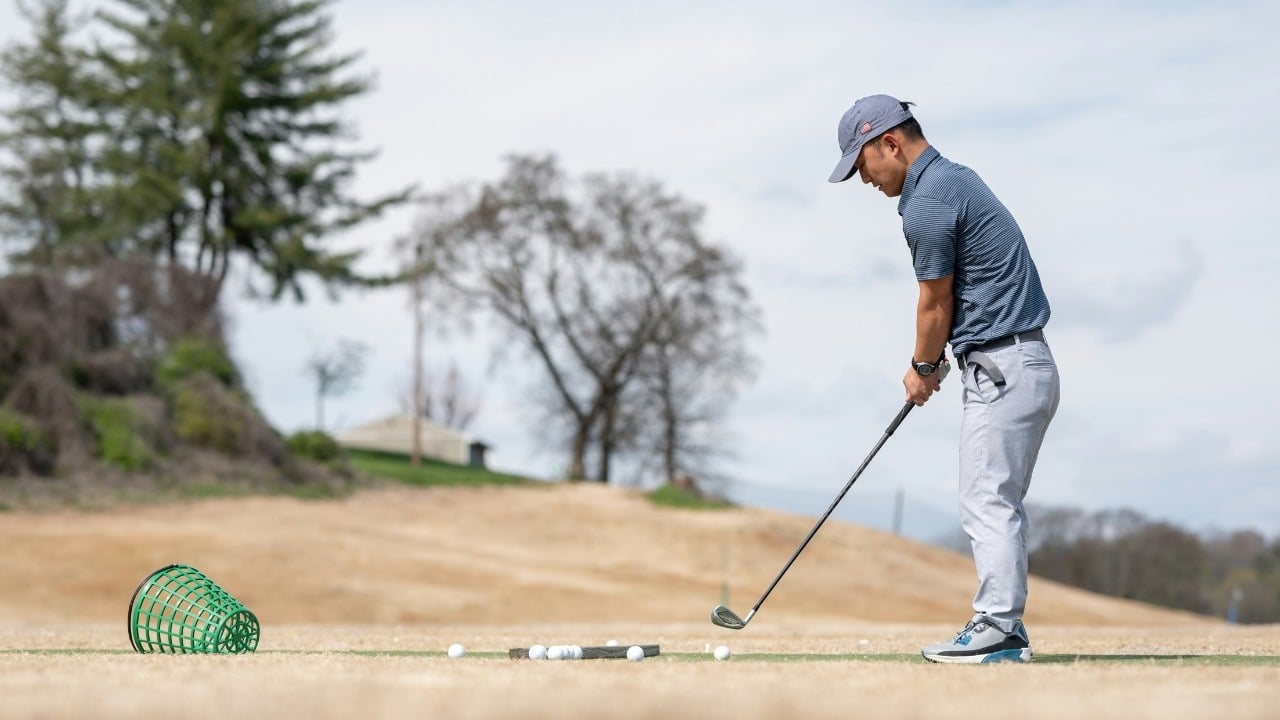 A man in a blue shirt and grey pants prepares to hit a golf ball.