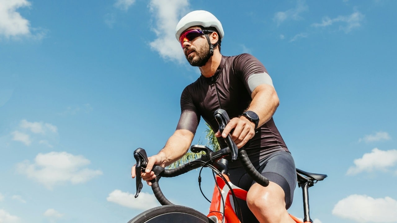 A man in cycling gear and a white helmet rides a bicycle against a blue sky.