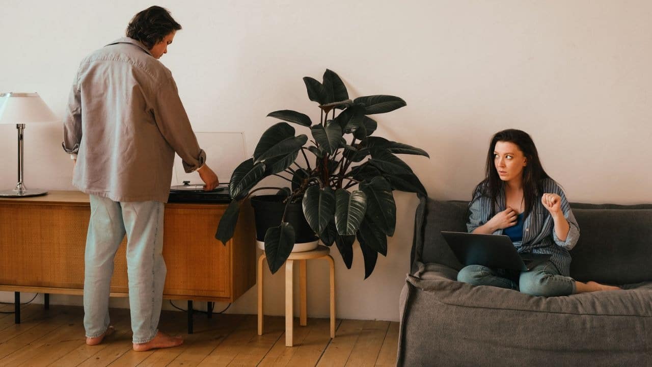 A person stands by a record player while another person sits on a sofa with a laptop.