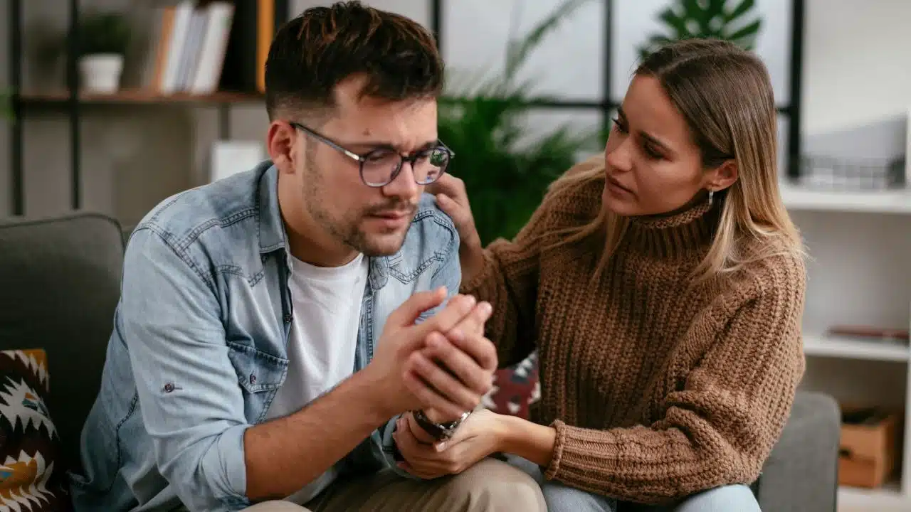 A woman places her hand on a man's shoulder while looking at him with concern.