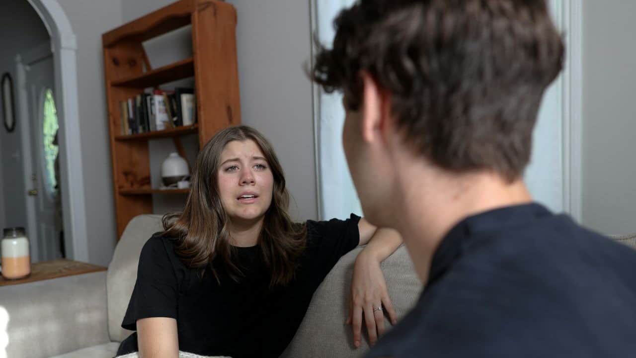 A woman with a tearful expression speaks to a person whose back is to the camera.