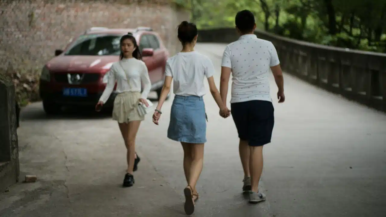 A couple walks away holding hands while another person walks toward them on a path.