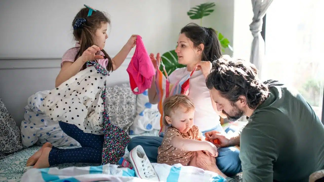 Two adults and two children sort through piles of colorful clothing on a bed.