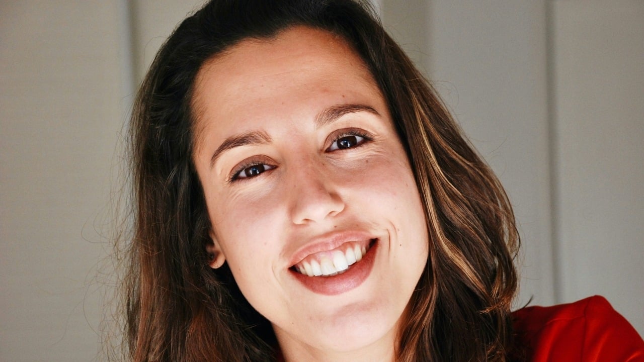 A close-up portrait of a woman with brown hair smiling directly at the camera.