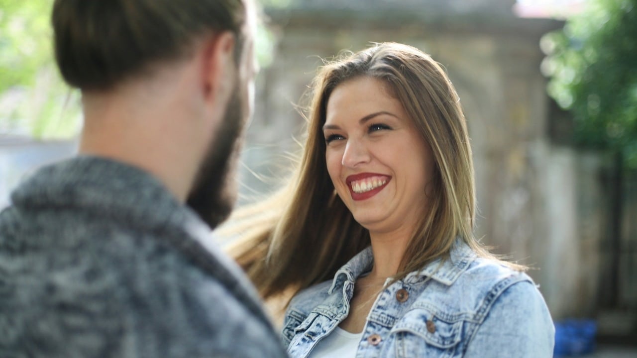 A man in a white shirt smiles warmly while looking at a woman sitting nearby.