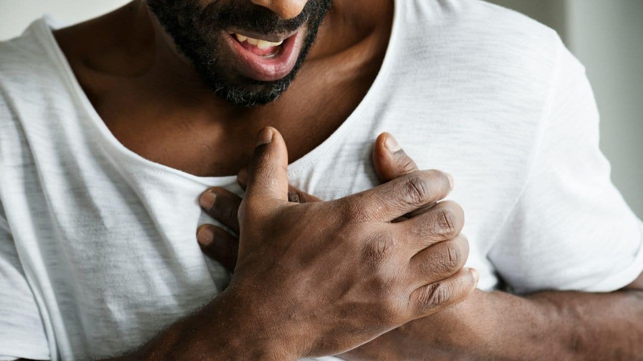 A man with a beard and a white shirt holds his hands tightly against his chest.
