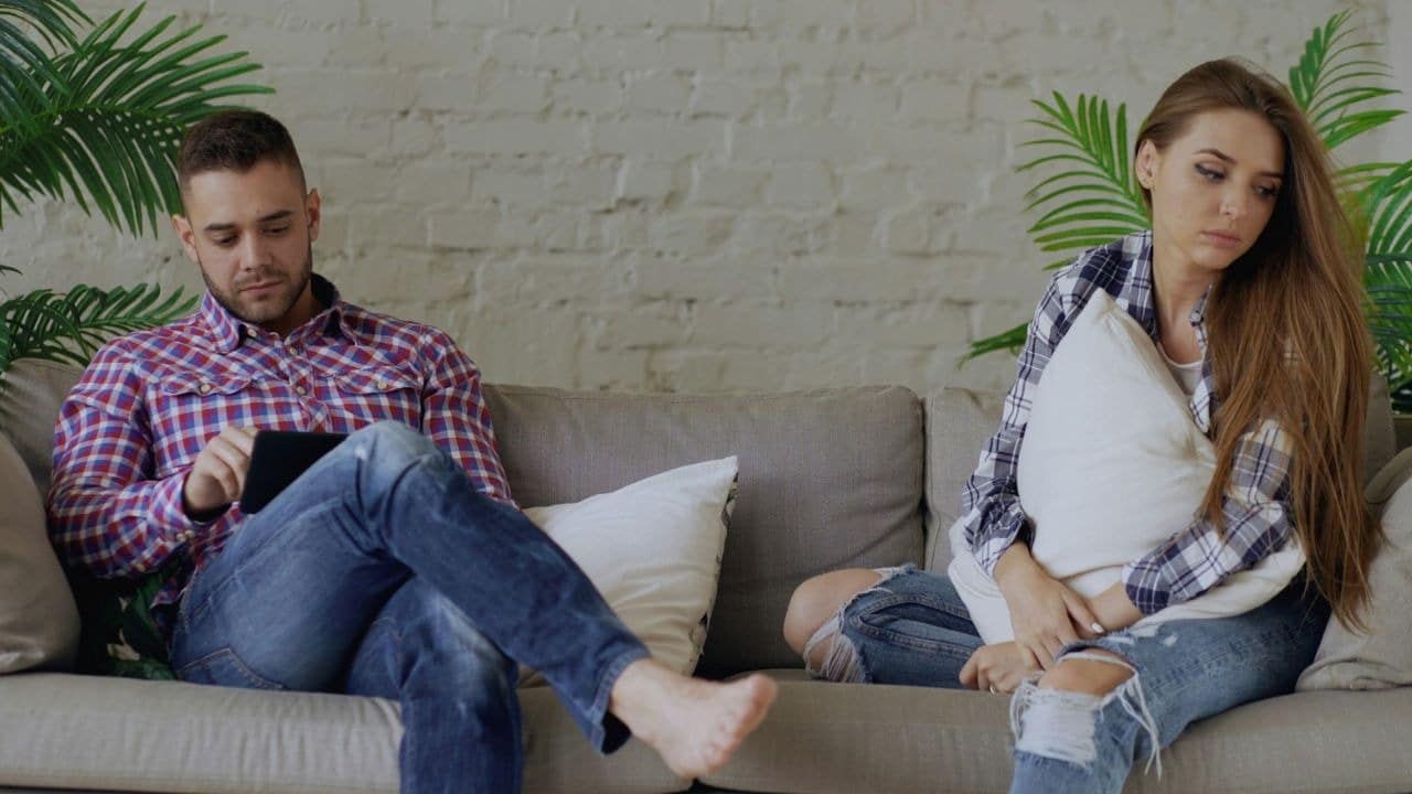 A man and woman sit on a sofa, looking in different directions without making eye contact.