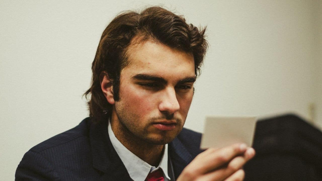 A man in a suit looks down with a serious expression at a small photo.