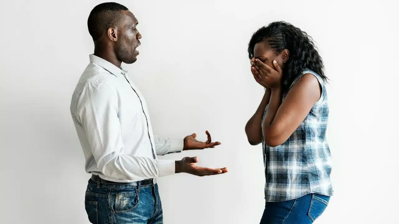 A man gestures with open hands toward a woman who is covering her face.