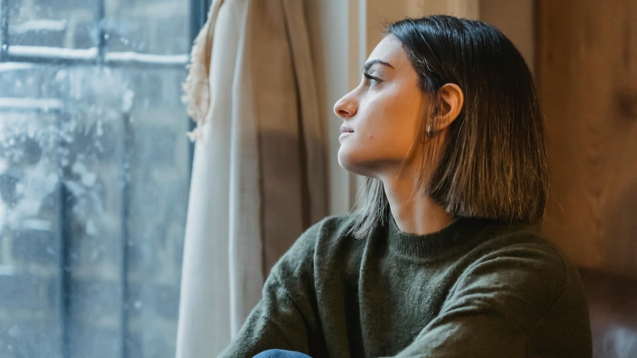 A person with short brown hair looks thoughtfully out of a window in profile.