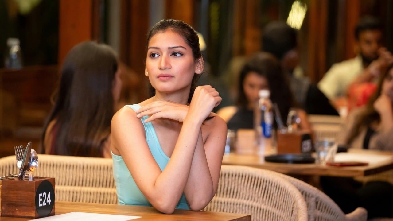 A woman in a light blue top sits at a wooden table in a crowded restaurant.