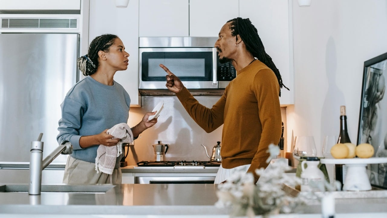 A man and woman stand in a kitchen having an intense, gesturing conversation.