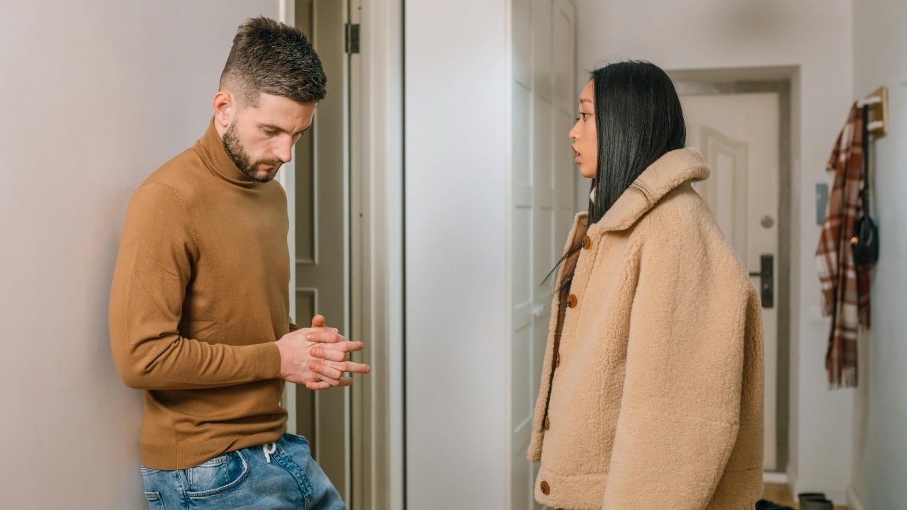 A man looks down while a woman in a tan coat speaks to him.