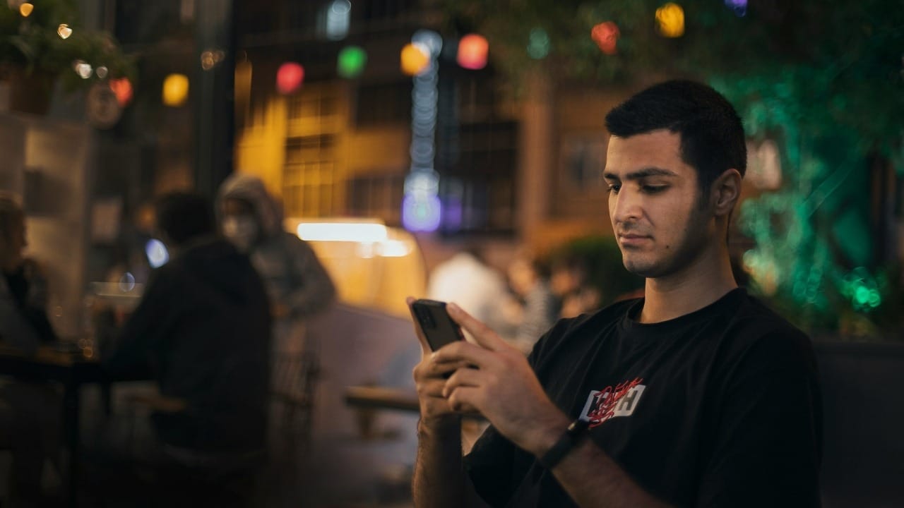 A man in a black shirt looks at his phone while sitting outdoors at night.