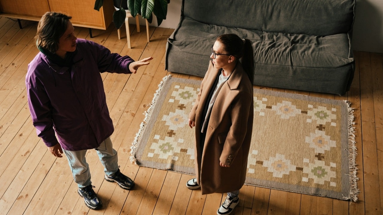 From a high angle, a man in a purple jacket gestures toward a standing woman.