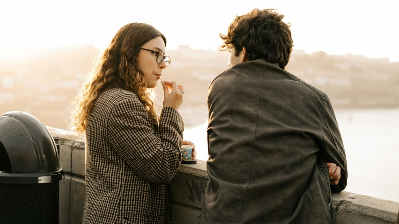 A woman in a patterned coat eats a snack while talking to a man outdoors.